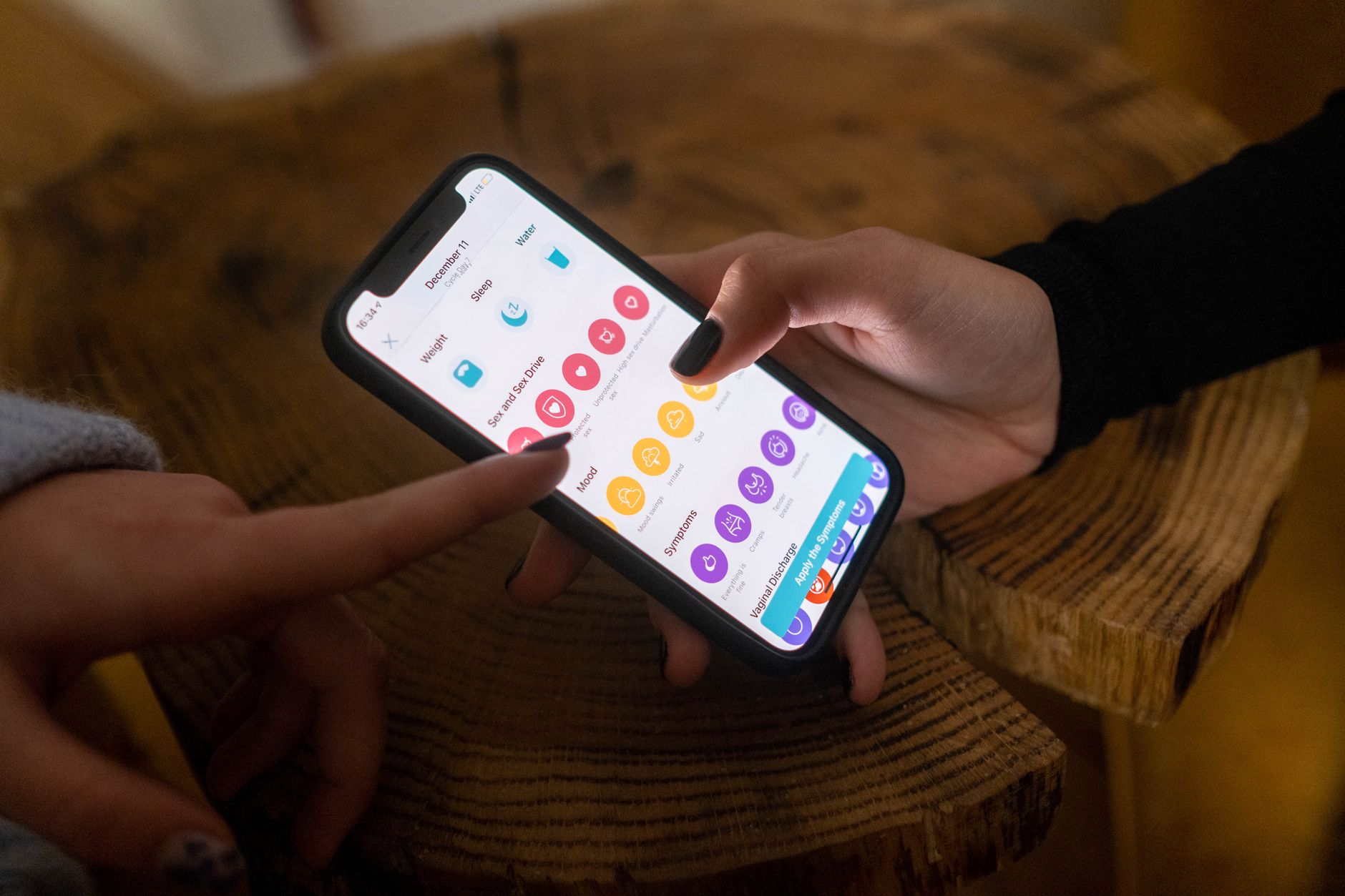 Deux personnes regardent ensemble l’écran d’une application ouverte sur un smartphone, autour d’une table en bois.